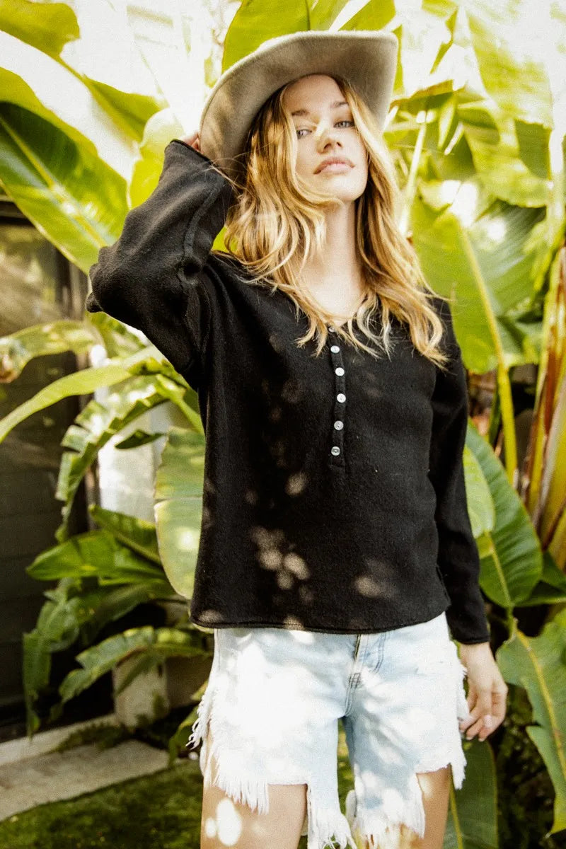 Woman wearing a black shirt and light denim shorts standing in front of large green leaves.