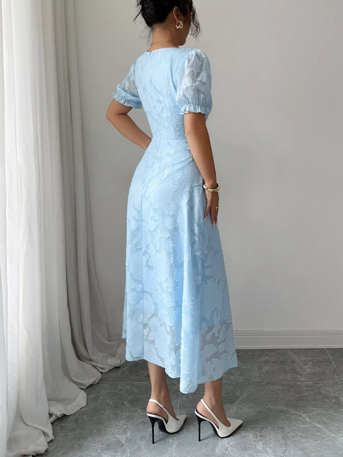 Woman wearing a light blue lace dress standing against a neutral background