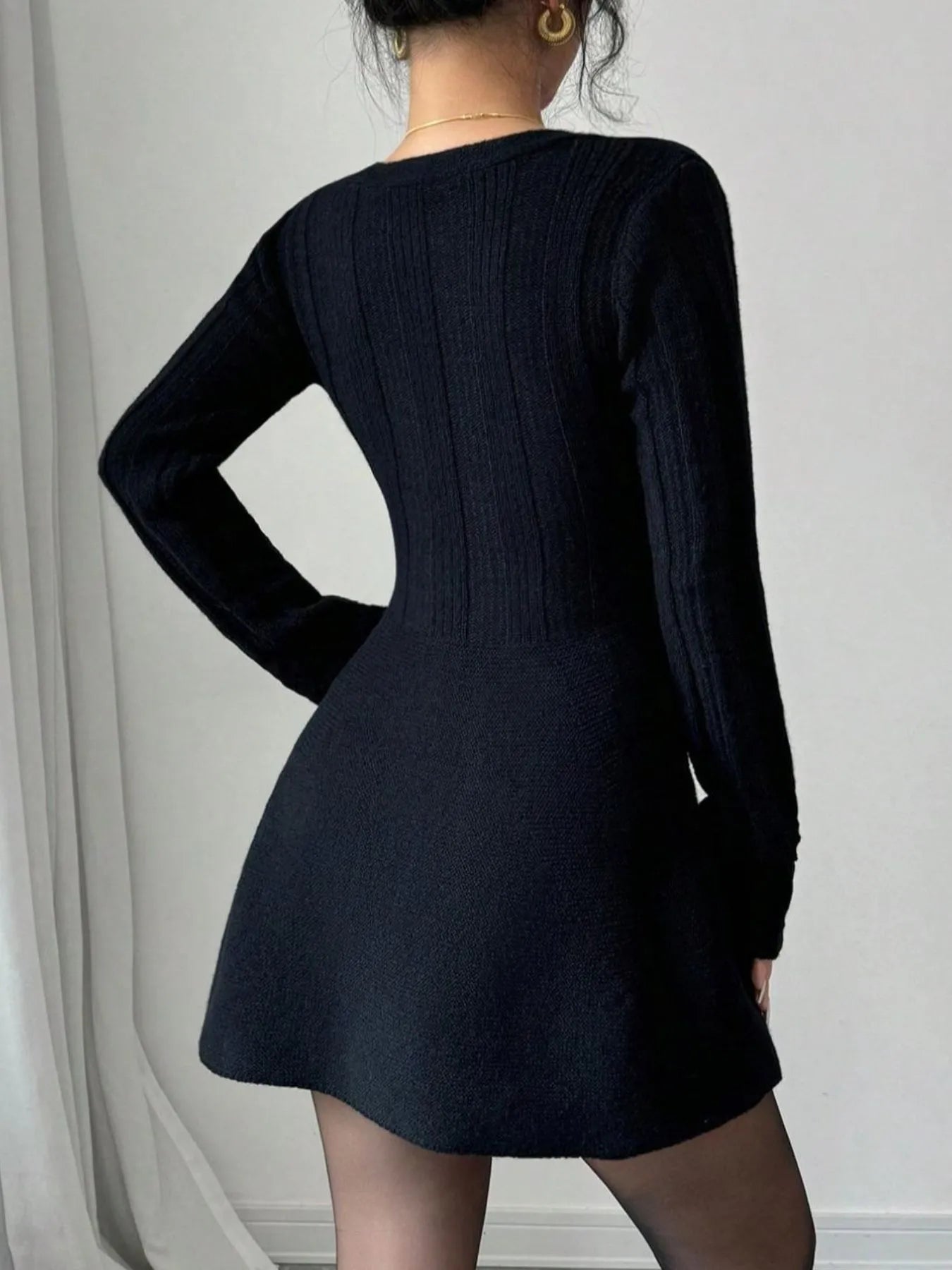 Person wearing a black dress with long sleeves against a plain background