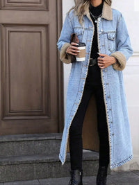 Person wearing a long denim coat with fur-lined cuffs, holding a coffee cup.