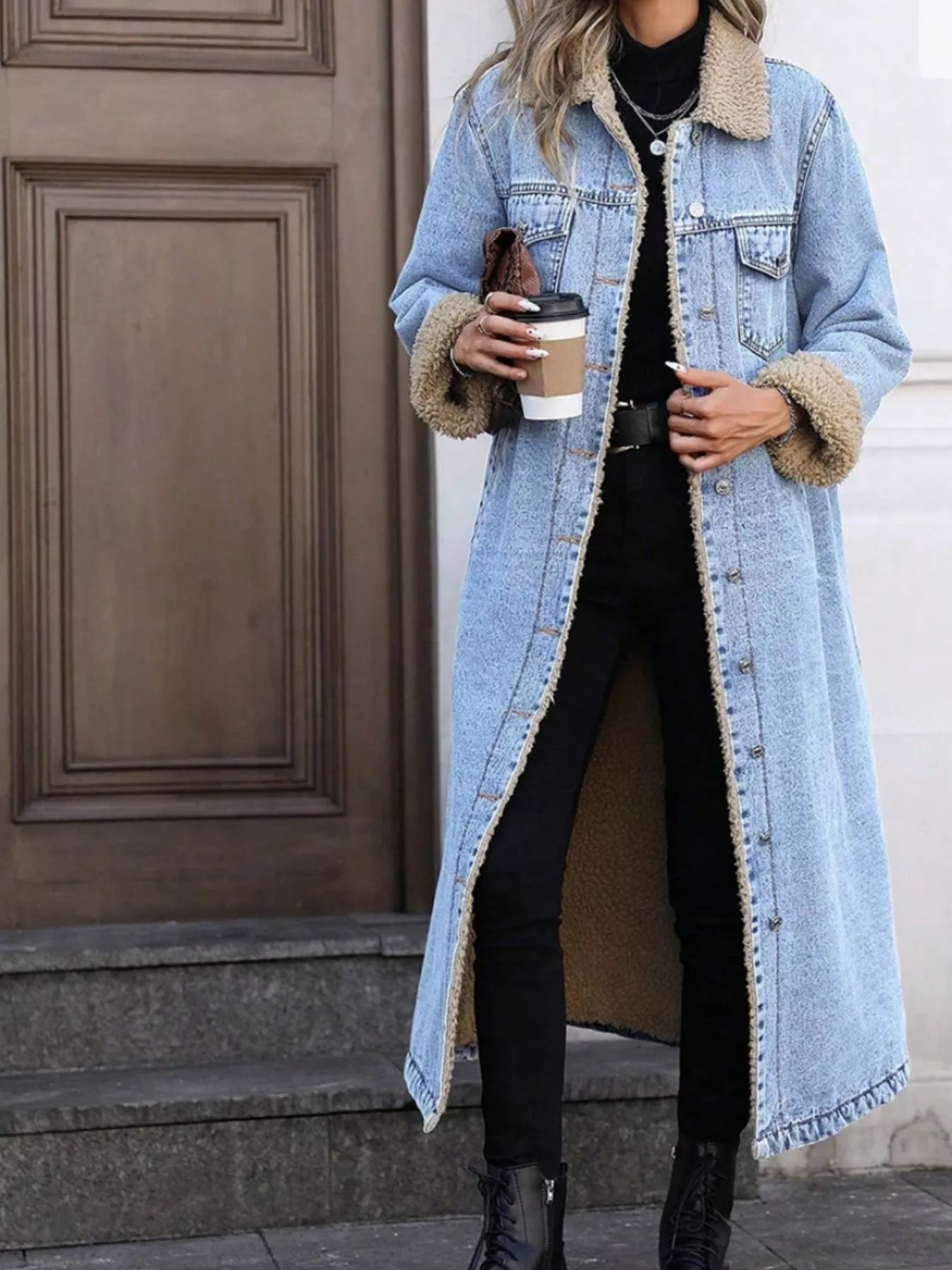 Person wearing a long denim coat with fur-lined cuffs, holding a coffee cup.