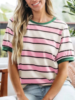 Woman wearing a striped shirt with pink, black, and green colors sitting indoors.