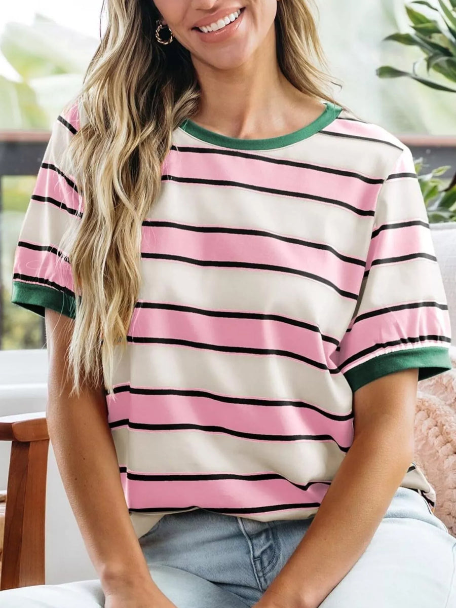 Woman wearing a striped shirt with pink, black, and green colors sitting indoors.