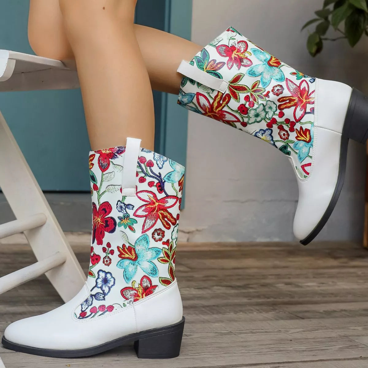 White boots with colorful floral patterns worn by a person sitting on a chair.