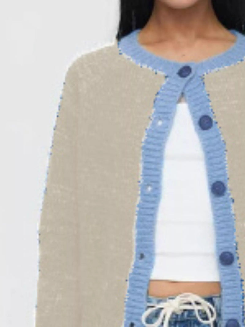 Blue knitted cardigan with button details over a beige sweater and white top on a plain background