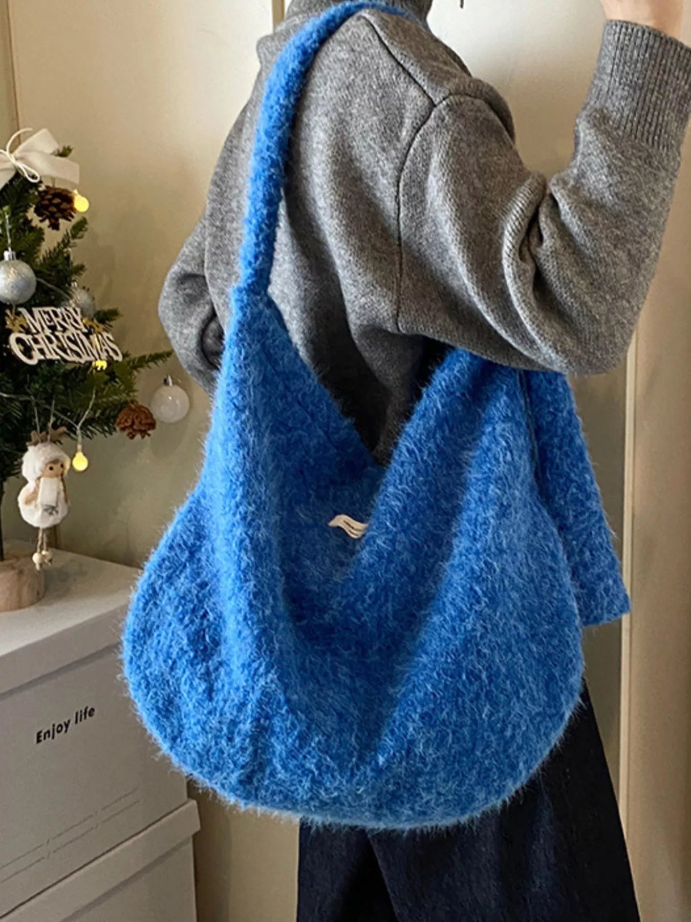 Person holding a blue fluffy bag with a Christmas tree and decorations in the background