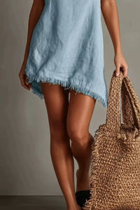Person wearing a light blue dress holding a woven bag against a neutral background