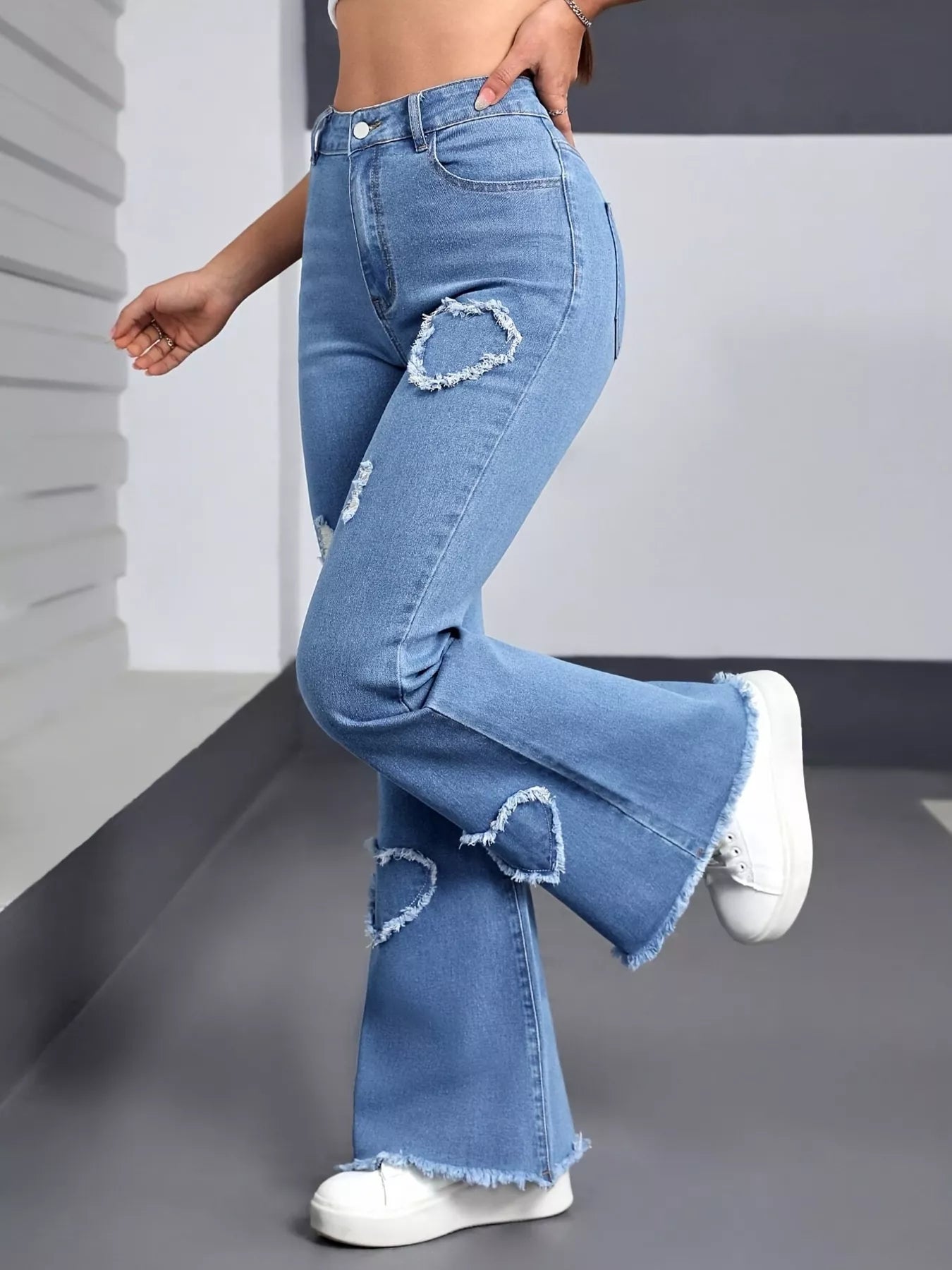Blue flared jeans with heart-shaped cutouts worn by a person on a neutral background