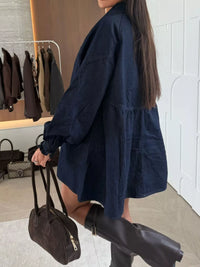 Woman wearing a navy blue dress with a white wall and clothing rack in the background