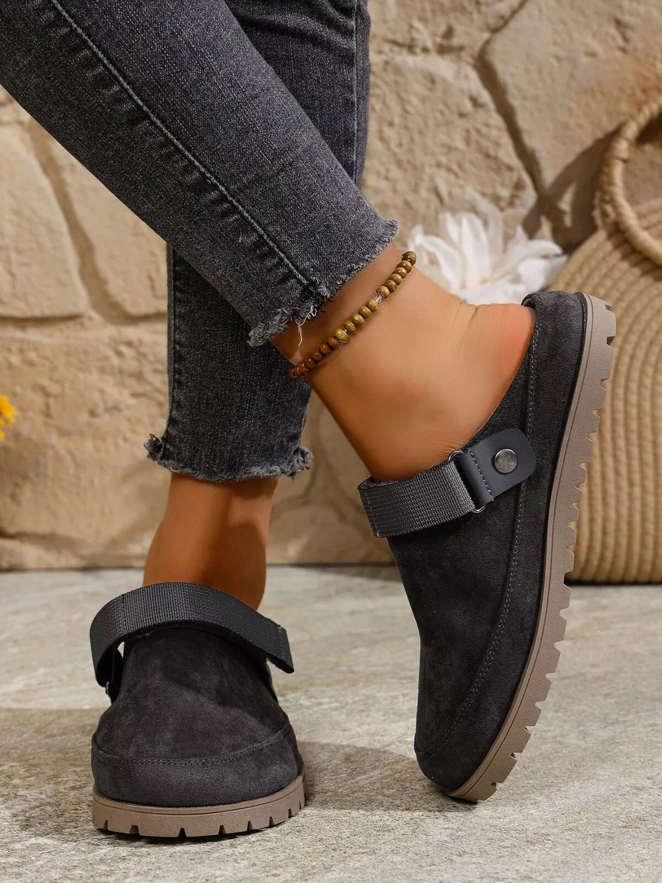 Black slip-on shoes worn with jeans against a stone wall background