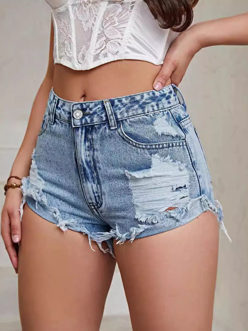 Person wearing distressed denim shorts and a white lace top against a neutral background
