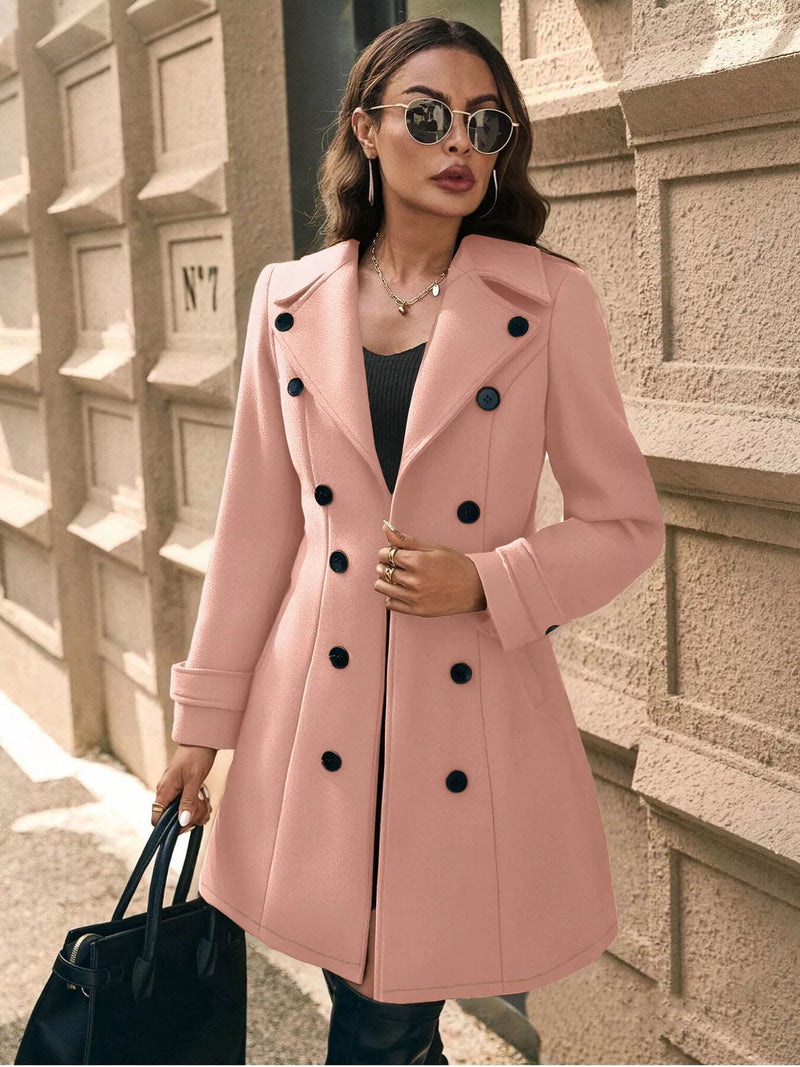 Woman wearing a pink coat with black buttons against a textured wall.