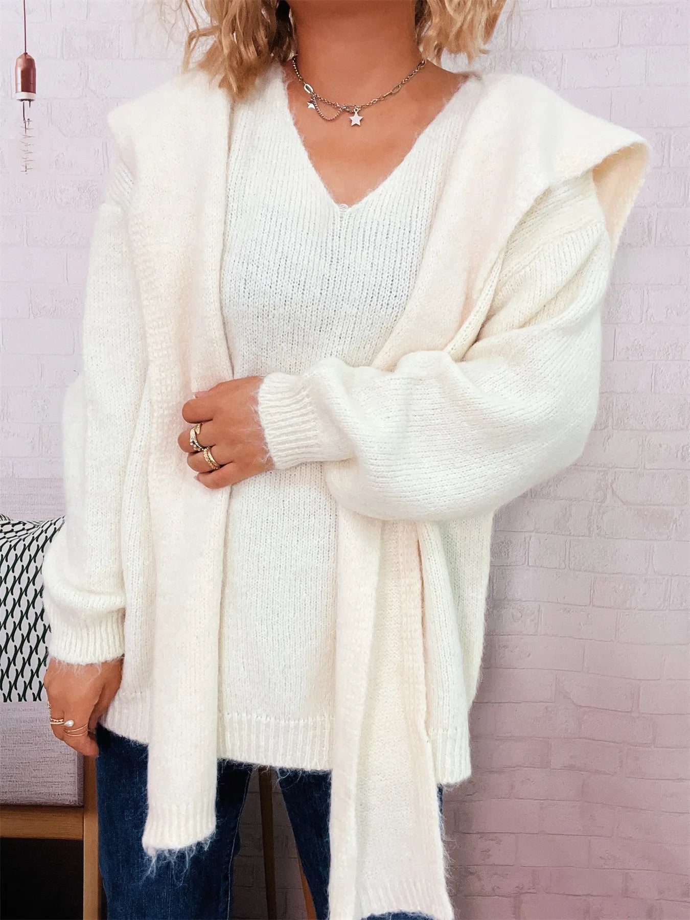 Person wearing a white cardigan over a white sweater with a blurred background