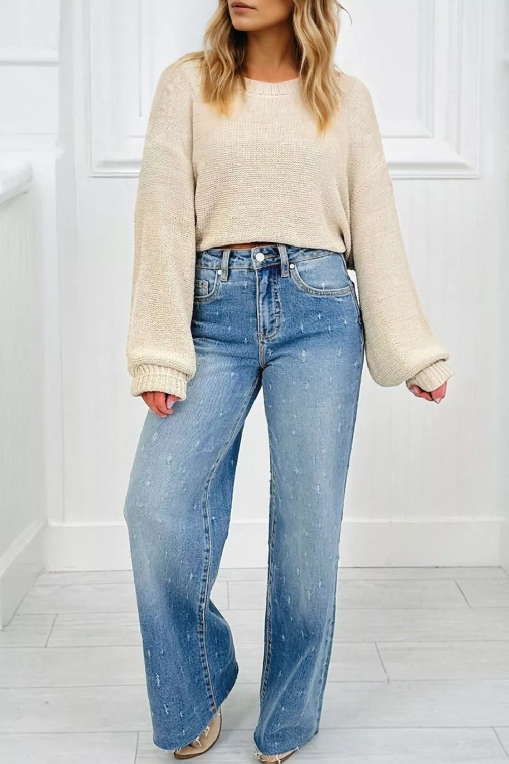 Person wearing a beige sweater and blue jeans in a minimalistic setting