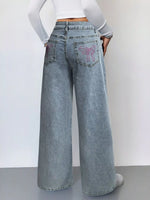 Person wearing light blue wide-leg jeans with decorative pocket designs on a plain background