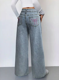 Person wearing light blue wide-leg jeans with decorative pocket designs on a plain background