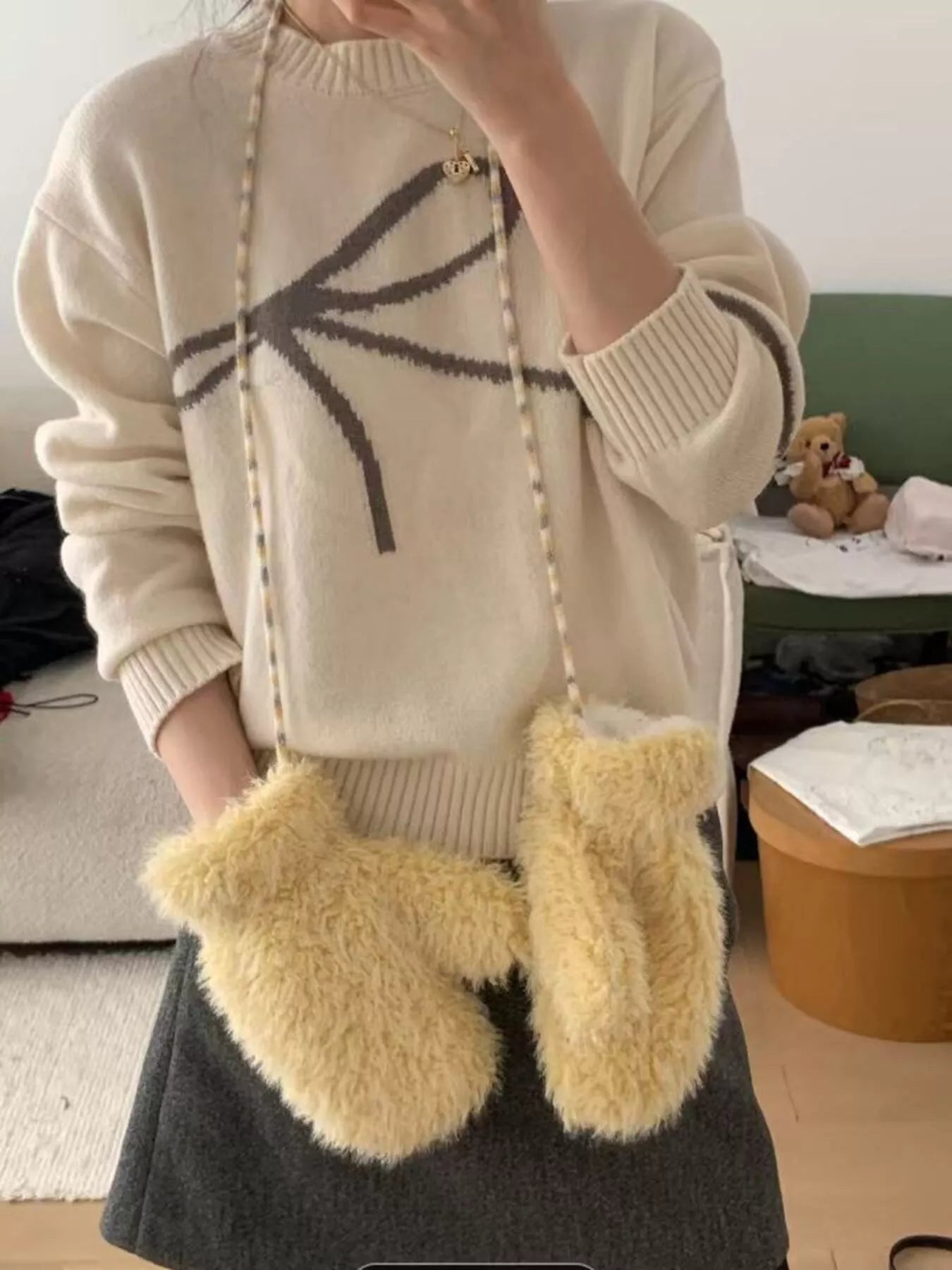 Person wearing a beige sweater with a black design and holding a fluffy yellow bag indoors.