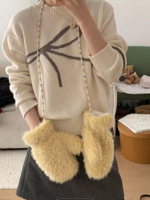 Person wearing a beige sweater with a black design and holding a fluffy yellow bag indoors.