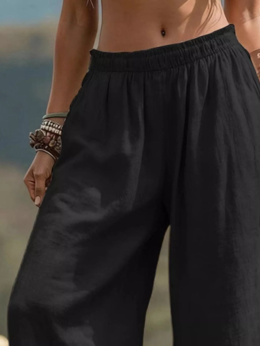 Black wide-leg linen pants with an elastic waistband, shown on a model in an outdoor setting.
