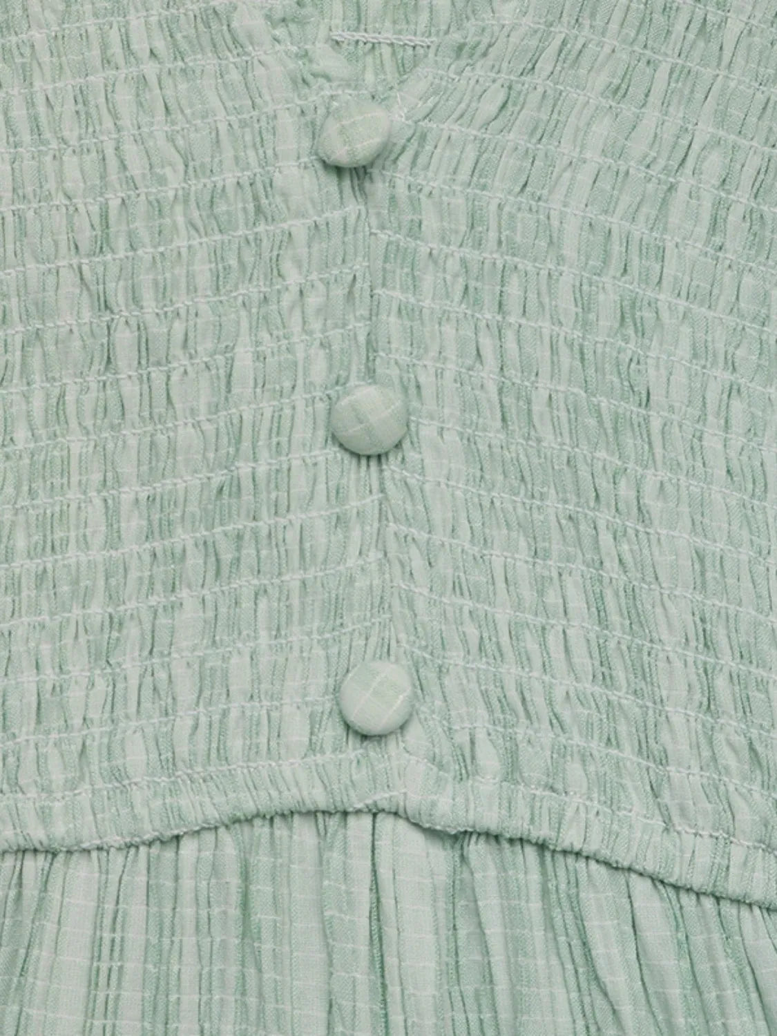Close-up of a light green textured fabric with buttons
