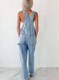 Person wearing a light blue denim jumpsuit against a white background