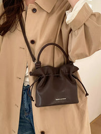 Person wearing a beige trench coat with a brown leather drawstring bag.