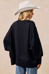 Person wearing a black oversized sweater and white cowboy hat on a beige background