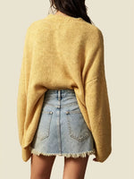 A person shown from the back wearing a loose, oversized yellow knit sweater and a light blue denim skirt with frayed hems, against a plain light beige background.