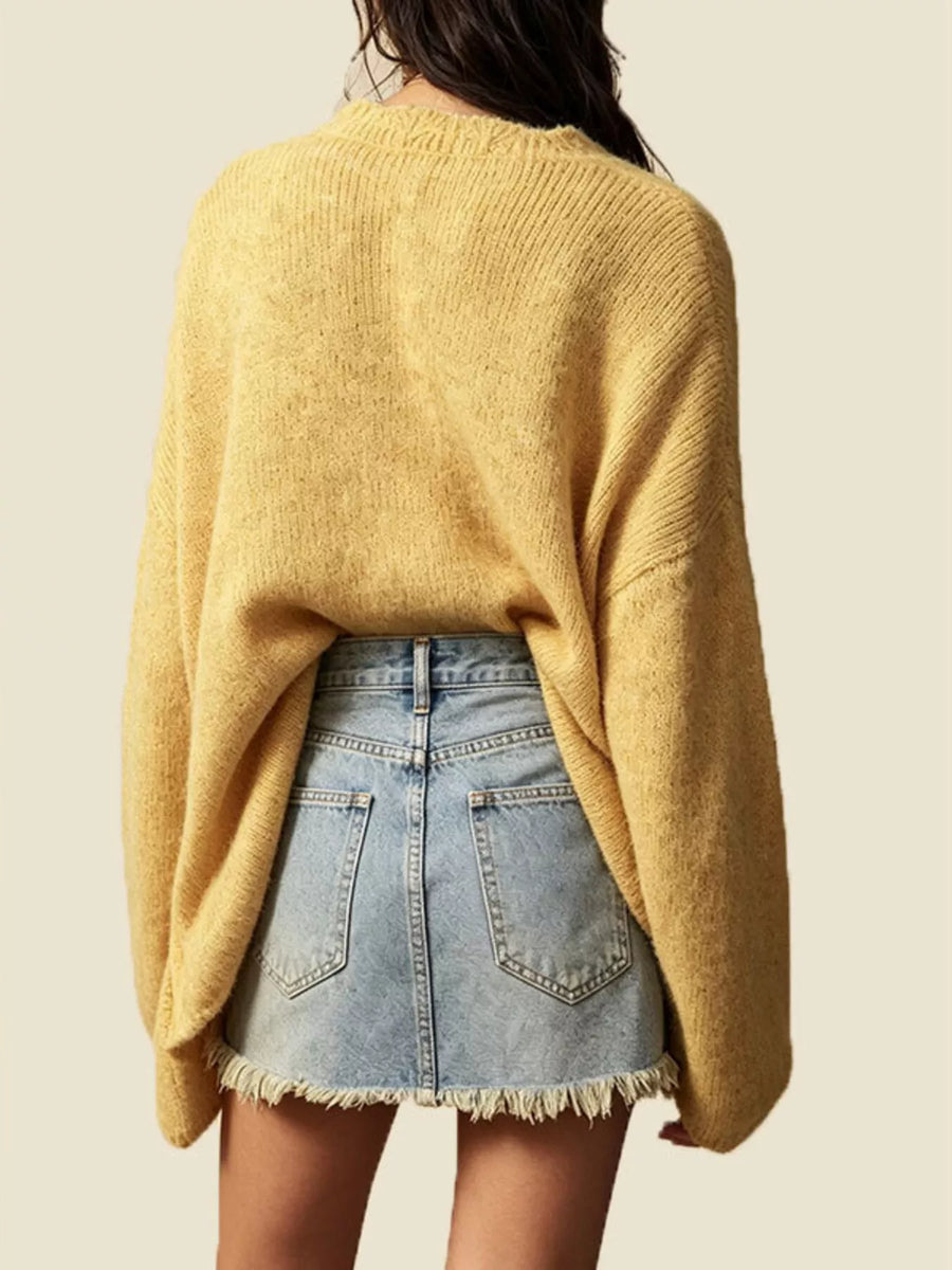 A person shown from the back wearing a loose, oversized yellow knit sweater and a light blue denim skirt with frayed hems, against a plain light beige background.