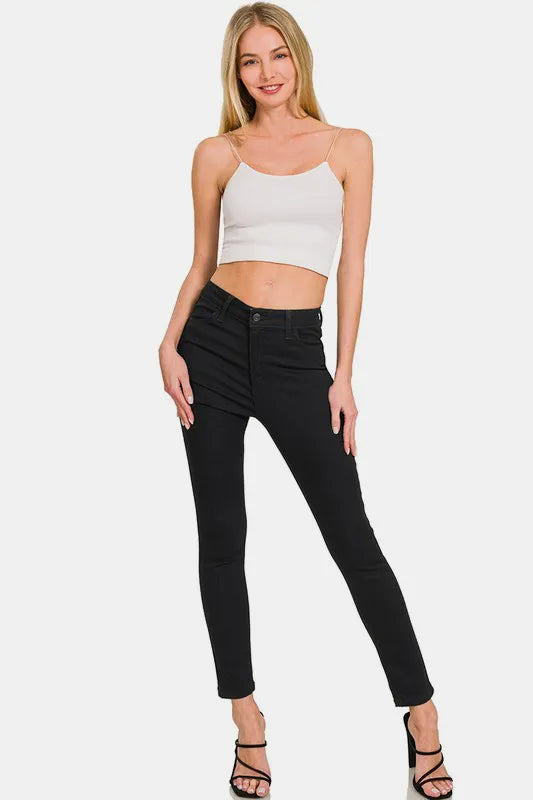 Woman wearing a white crop top and black high-waisted jeans on a white background