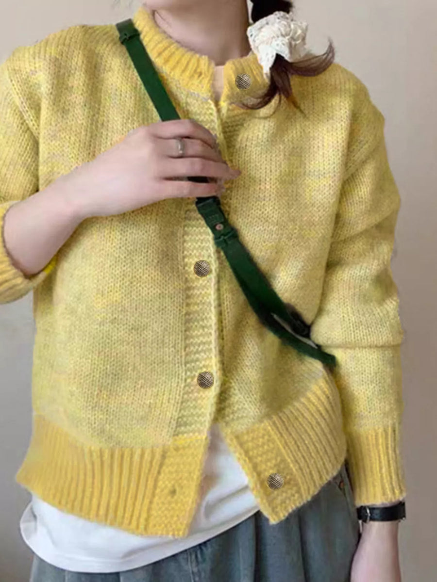 Person wearing a yellow knitted cardigan with a green strap over their shoulder against a plain background