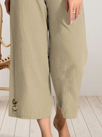 Beige wide-leg pants with buttons on a light wooden floor.