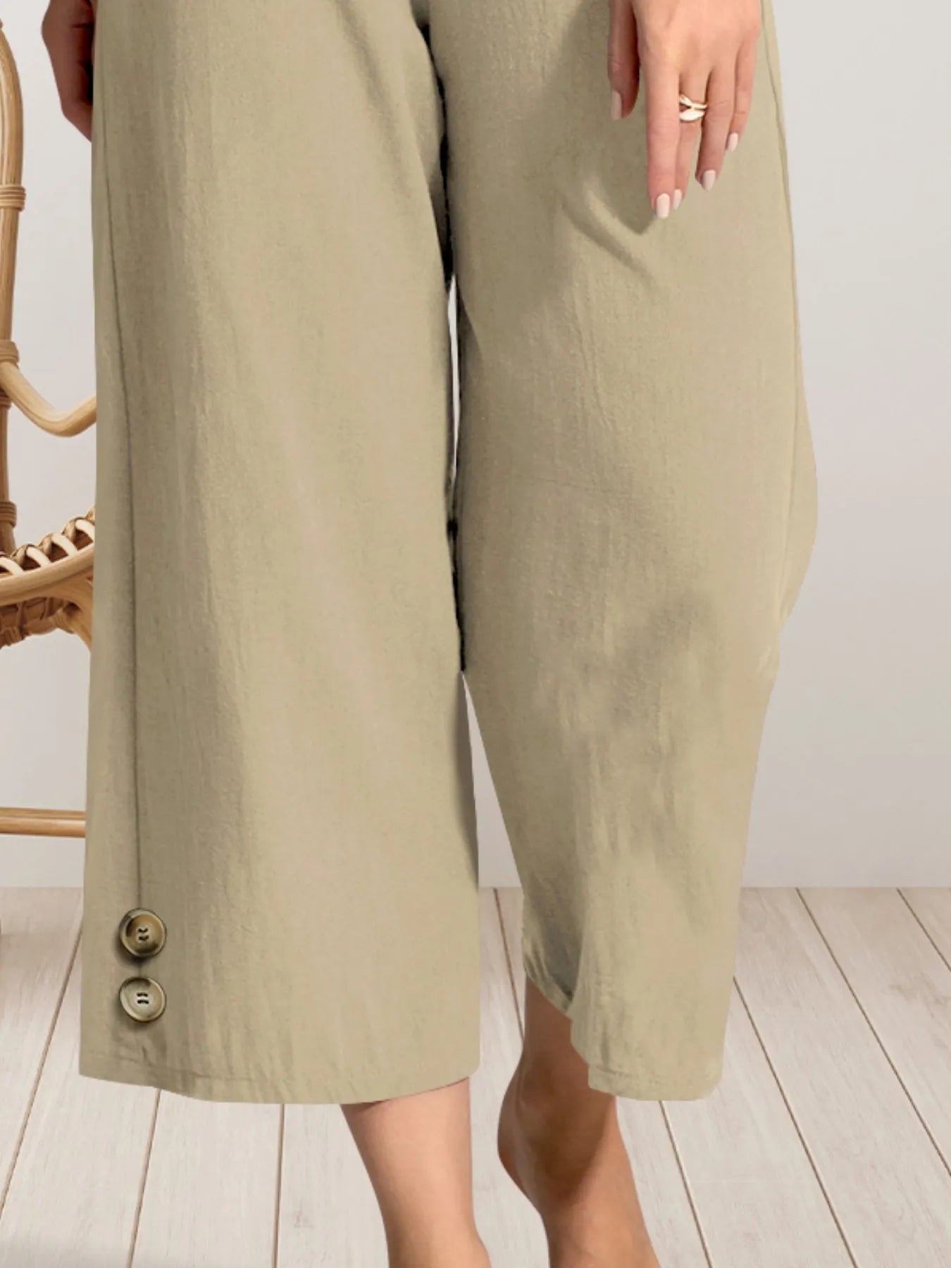 Beige wide-leg pants with buttons on a light wooden floor.