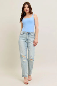 Woman wearing a light blue sleeveless top and light blue jeans on a beige background