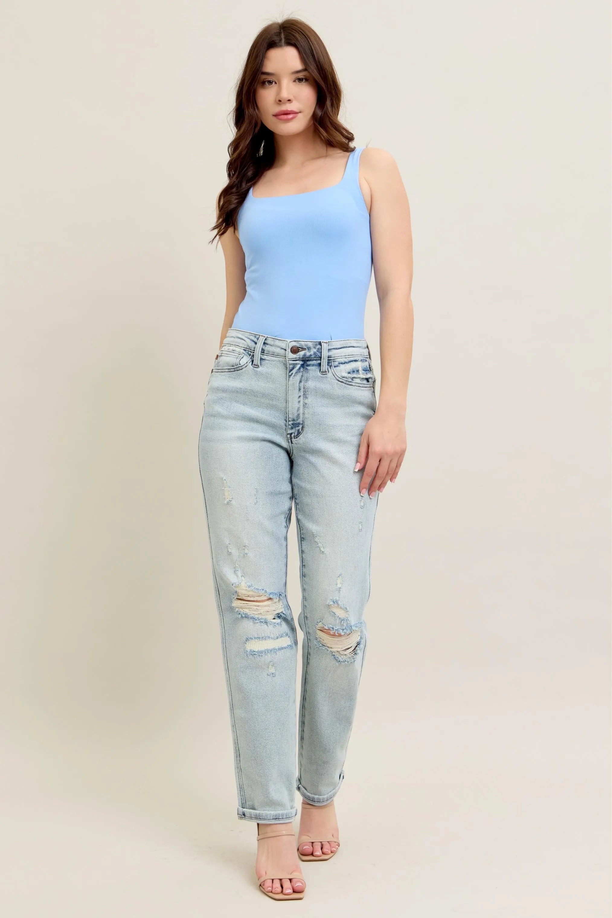Woman wearing a light blue sleeveless top and light blue jeans on a beige background