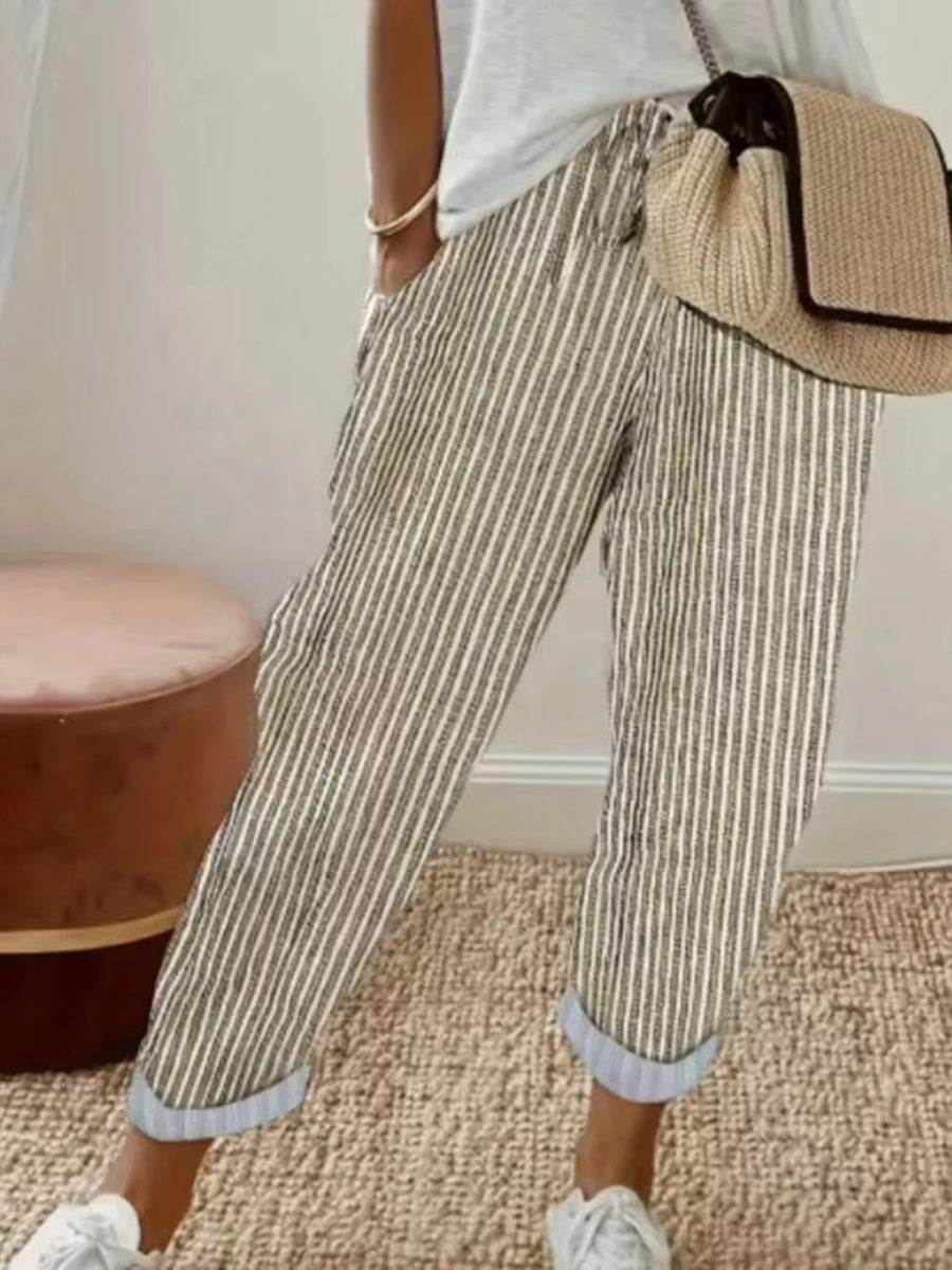 Person wearing striped pants with a beige bag and white sneakers in a room.