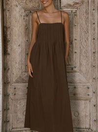 Woman wearing a brown dress standing in front of a wooden door.