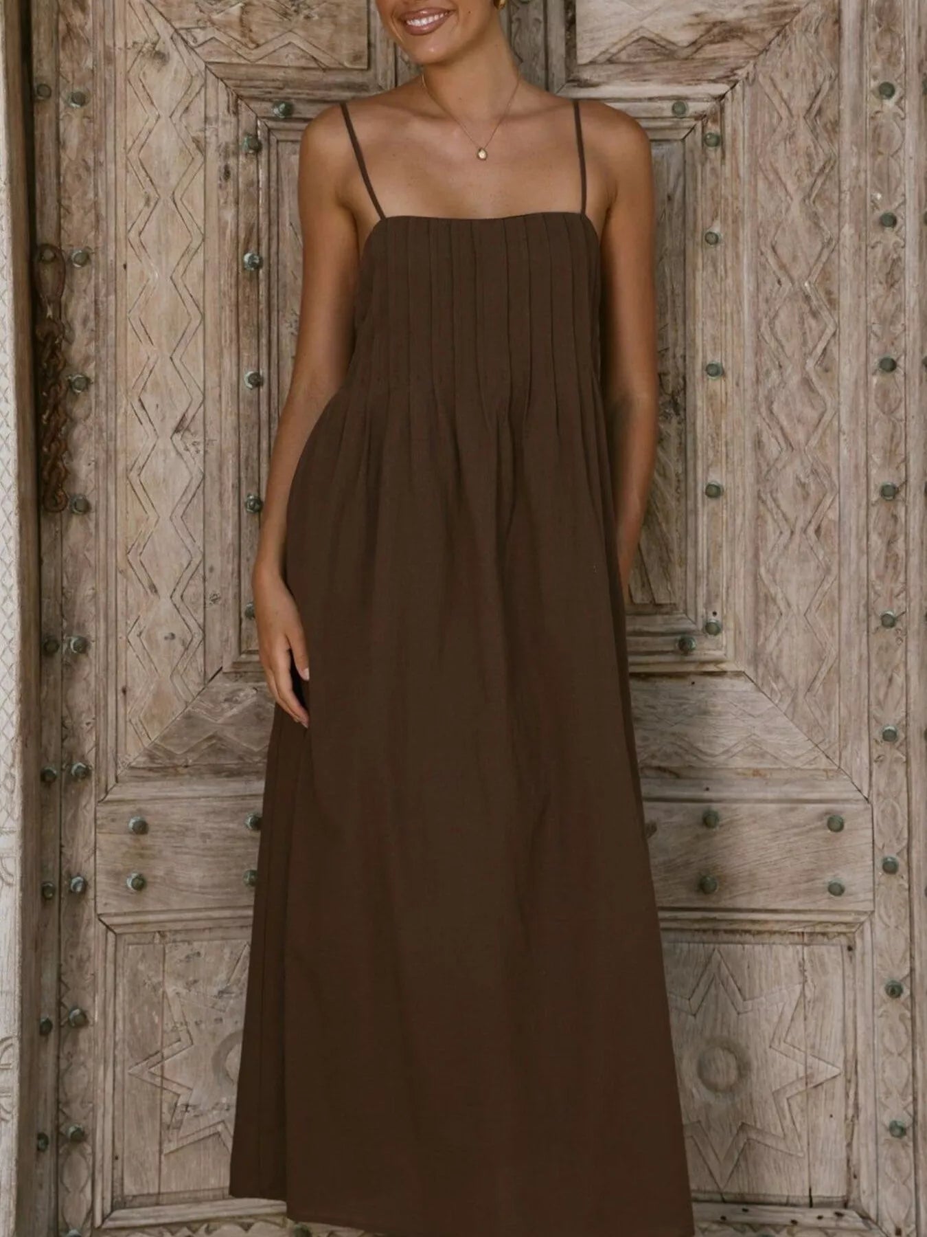 Woman wearing a brown dress standing in front of a wooden door.