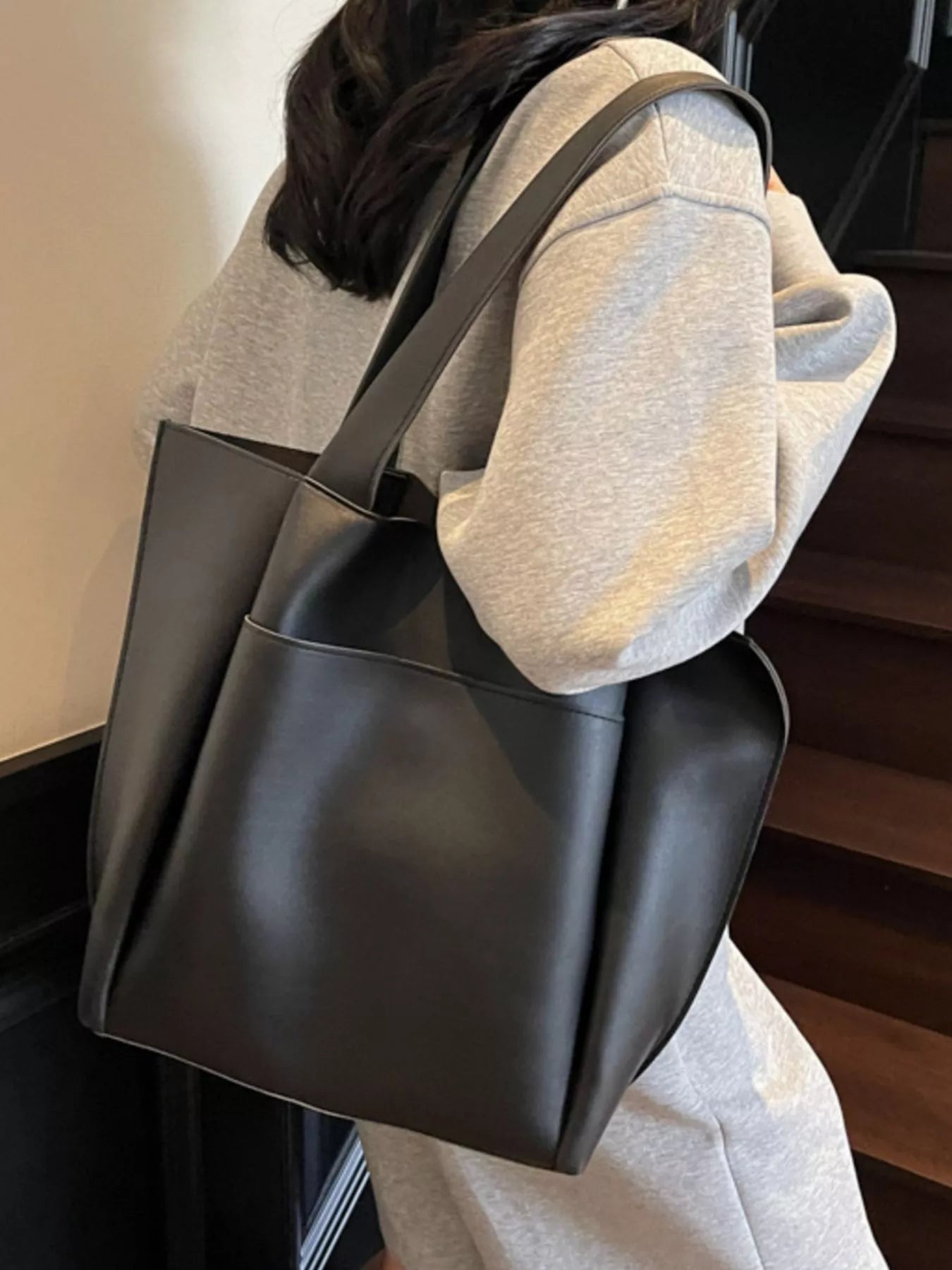 Person holding a black leather tote bag indoors