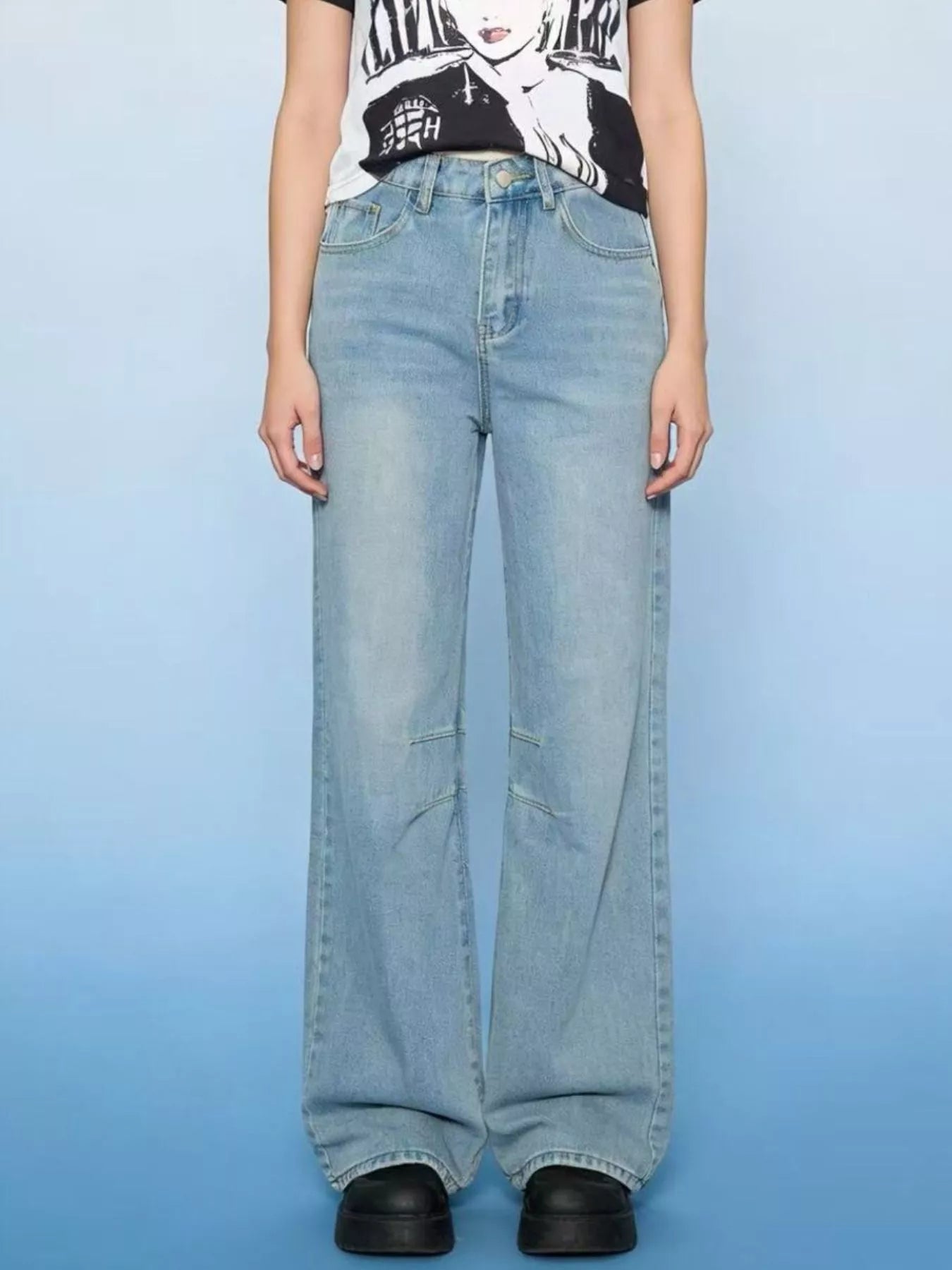 Person wearing light blue jeans and a graphic t-shirt on a solid background