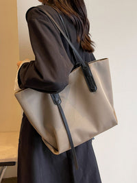 Person holding a beige tote bag with a black strap against a neutral background