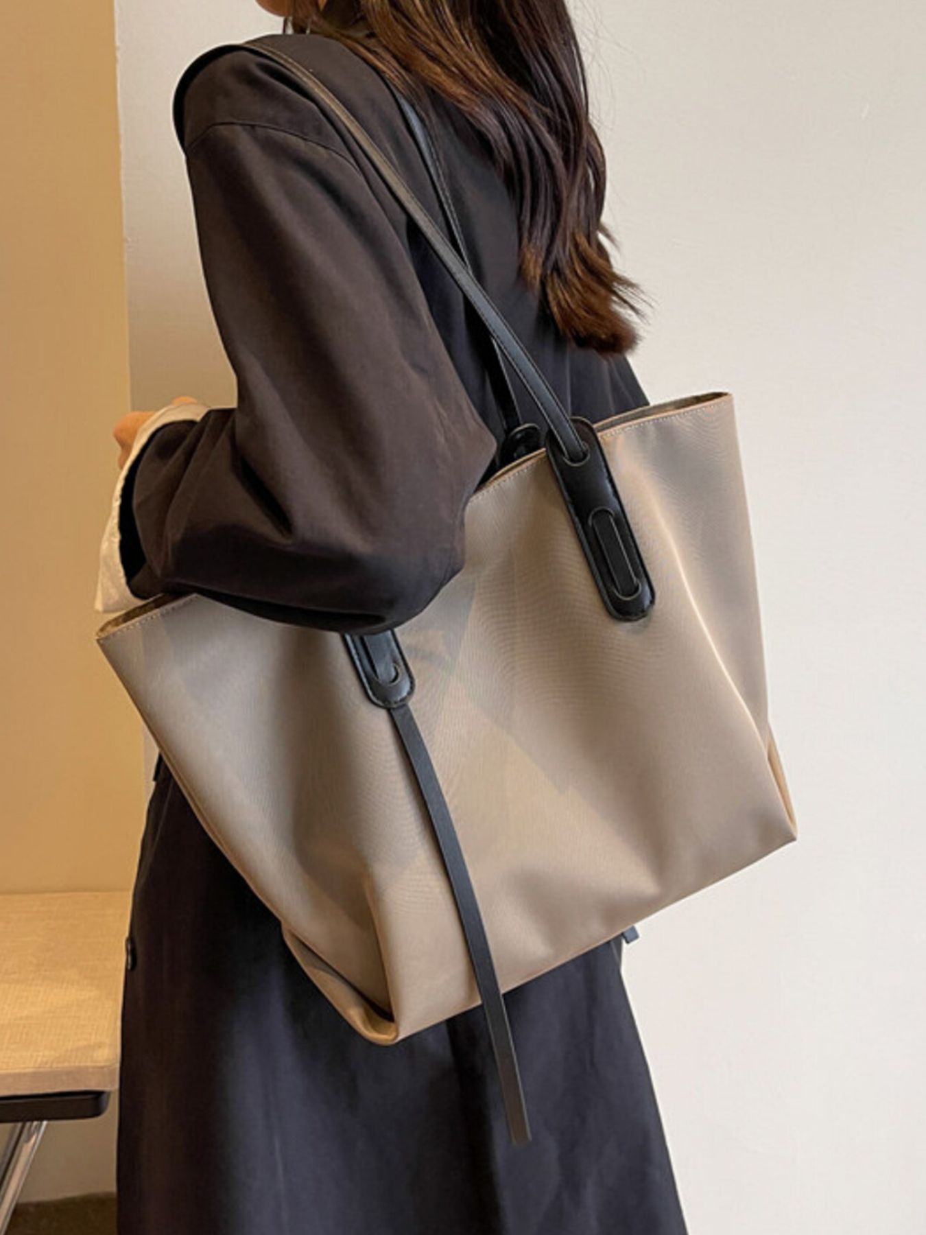 Person holding a beige tote bag with a black strap against a neutral background