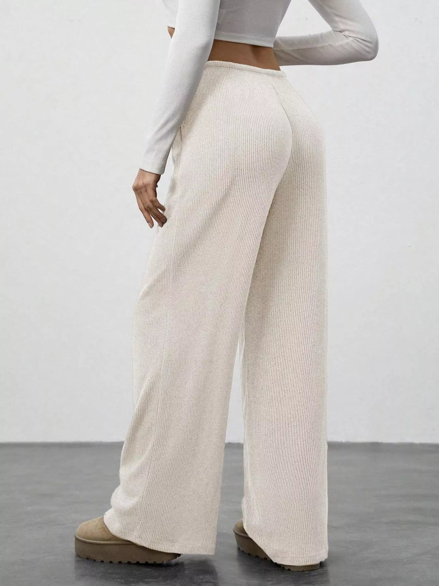 Person wearing beige ribbed wide-leg pants with a plain background