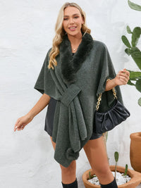 Woman wearing a dark gray poncho with fur trim against a white background