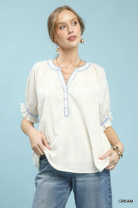 Woman wearing a cream blouse with blue accents and jeans on a light blue background