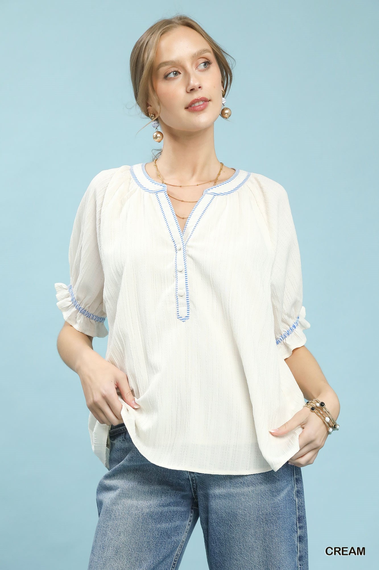 Woman wearing a cream blouse with blue accents and jeans on a light blue background
