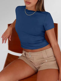 Person wearing a blue crop top and beige shorts sitting on a wooden chair.
