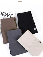 Four pairs of folded leggings in different colors (black, brown, dark gray, and beige) arranged on a white background with a magazine prop.