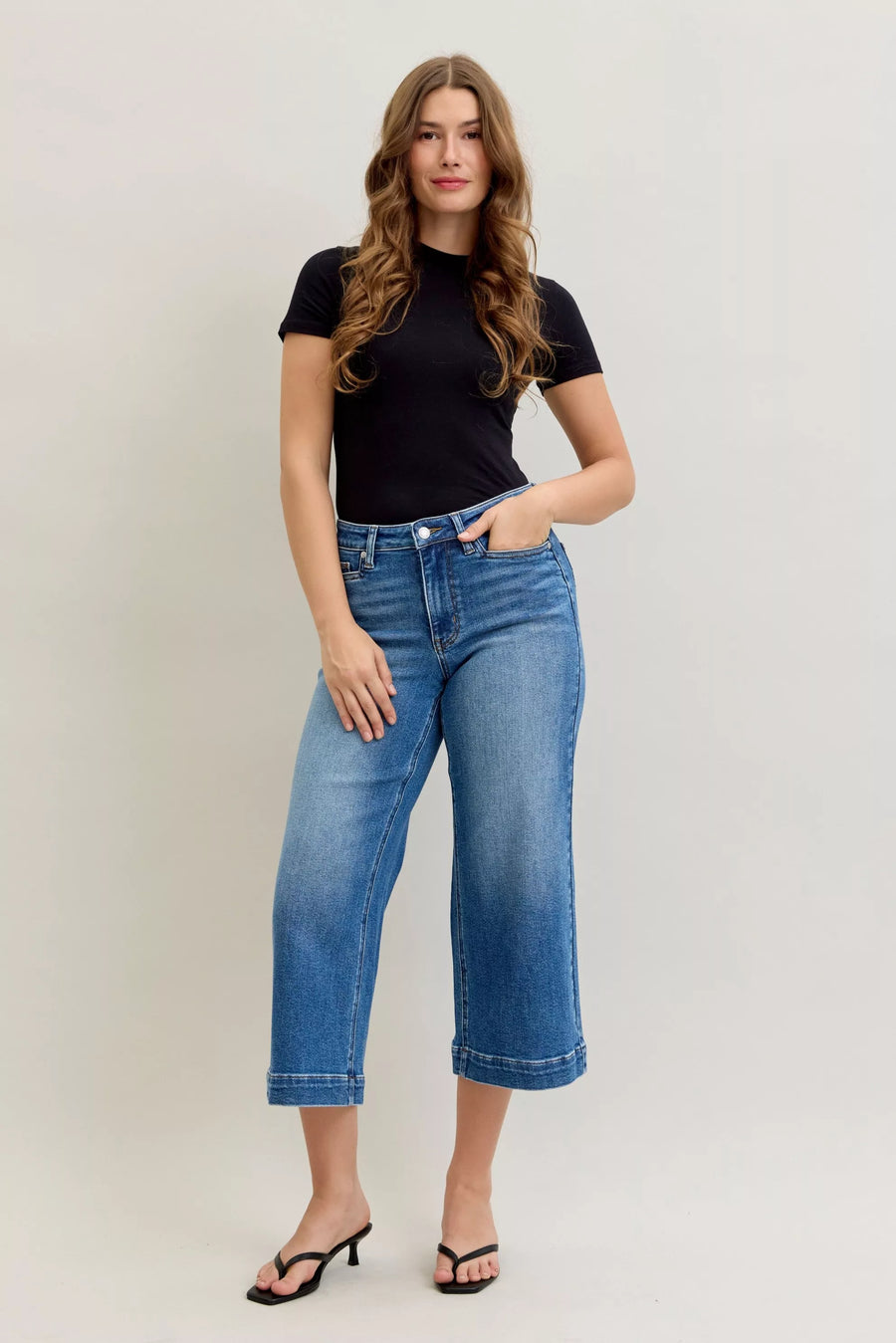 Woman wearing a black t-shirt and blue jeans against a plain background