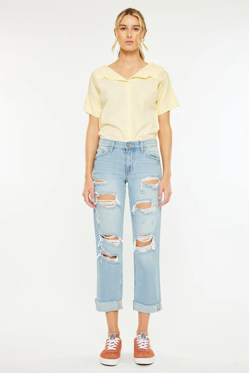 Woman wearing a yellow top and light blue ripped jeans on a white background